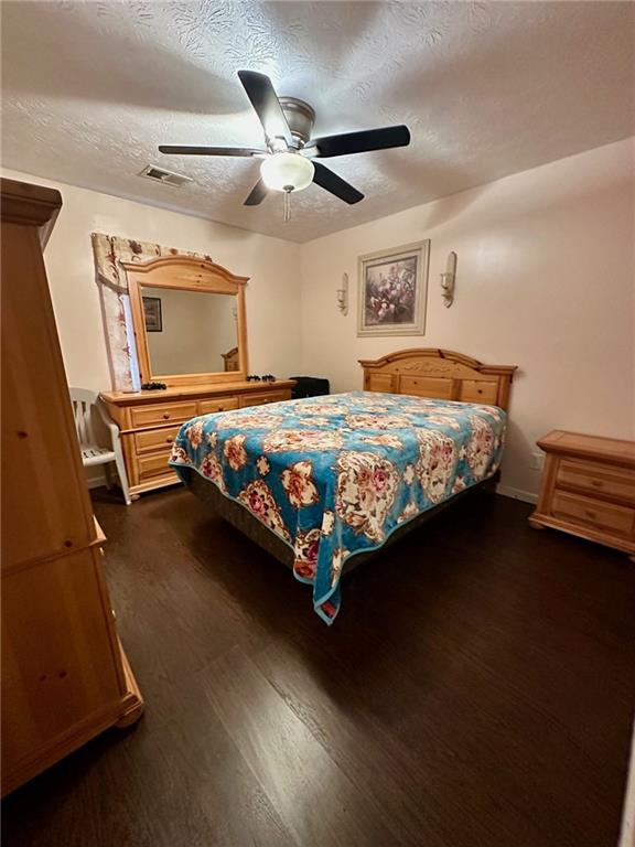 bedroom featuring dark wood-type flooring, a textured ceiling, and ceiling fan