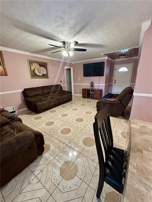 living room featuring ceiling fan, crown molding, and a textured ceiling