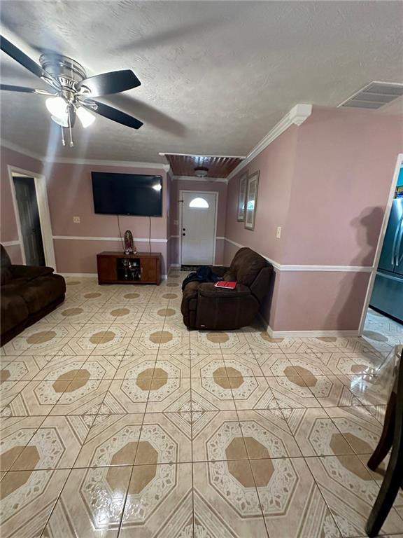 living room featuring ceiling fan, ornamental molding, and a textured ceiling