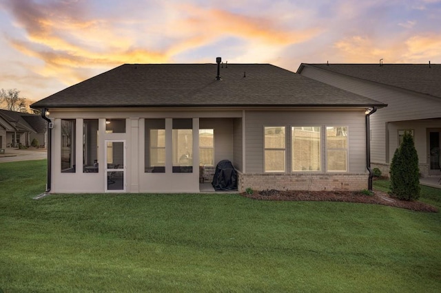 back house at dusk featuring a lawn