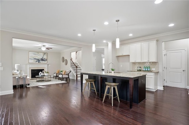 kitchen with a sink, light stone counters, tasteful backsplash, dark wood-style floors, and white cabinets