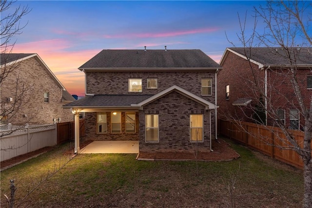 back of property at dusk with a yard, a patio, brick siding, and a fenced backyard