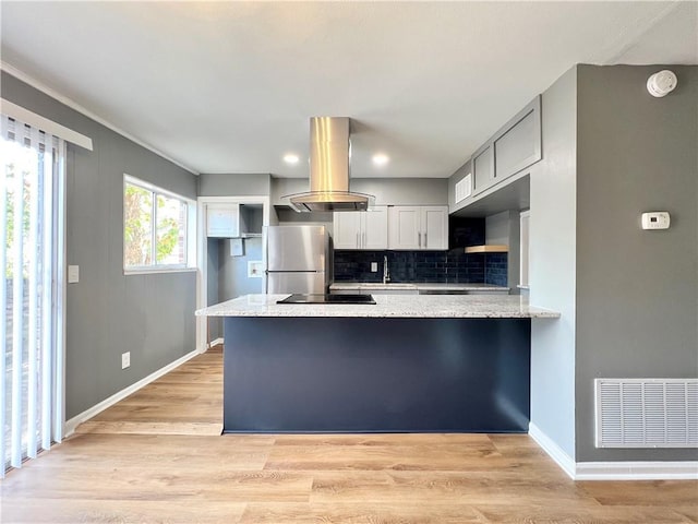 kitchen with visible vents, island exhaust hood, freestanding refrigerator, light wood-style floors, and a peninsula