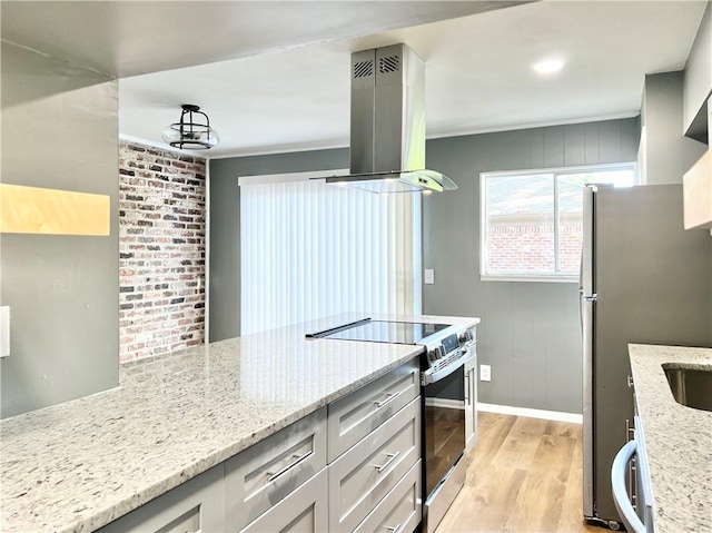 kitchen featuring light stone counters, baseboards, island exhaust hood, stainless steel appliances, and light wood-type flooring