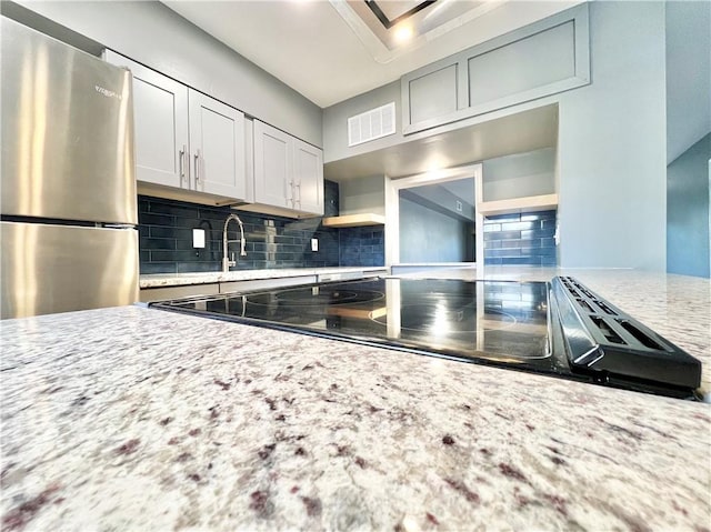 kitchen featuring visible vents, open shelves, freestanding refrigerator, decorative backsplash, and light stone countertops