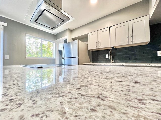 kitchen with decorative backsplash, light stone countertops, white cabinets, and freestanding refrigerator