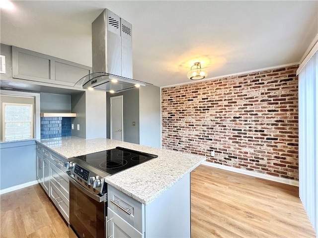 kitchen featuring brick wall, a peninsula, island exhaust hood, light wood-style floors, and electric range