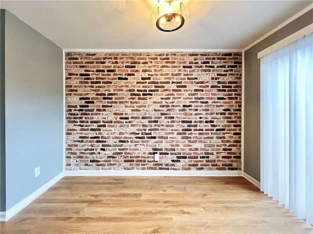 unfurnished room with light wood-style flooring, brick wall, crown molding, and baseboards