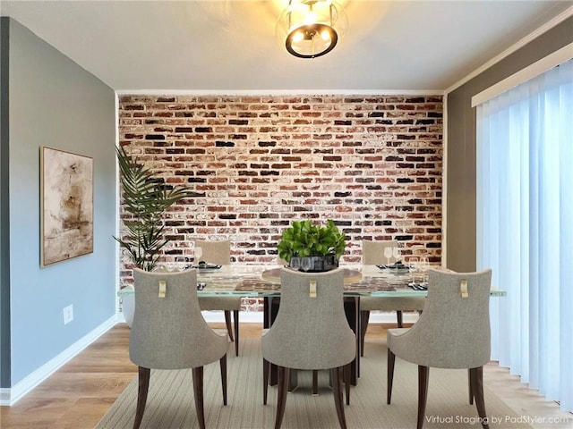 dining area featuring light wood finished floors, brick wall, and baseboards