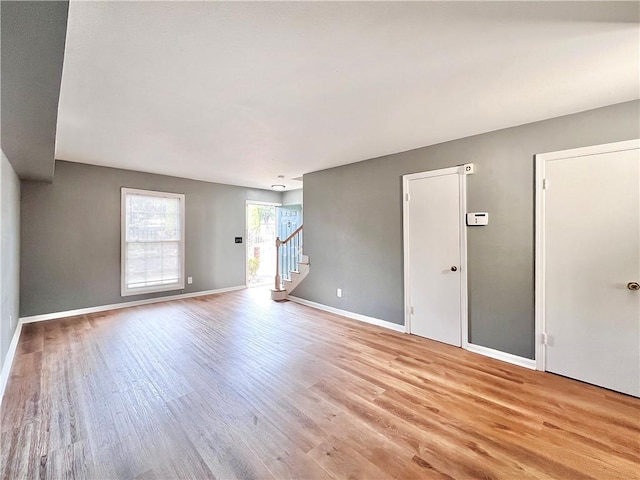 unfurnished living room with stairway, baseboards, and light wood-type flooring