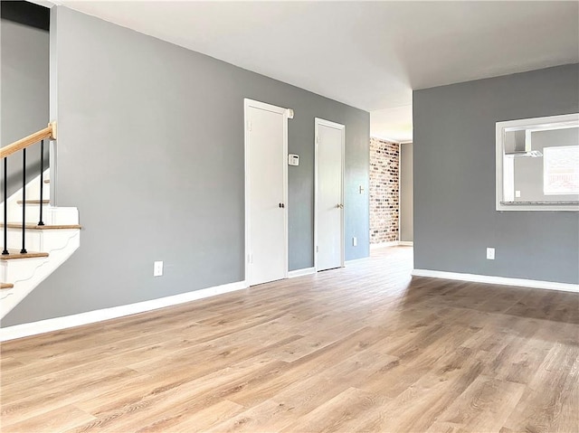 empty room with stairway, baseboards, and light wood-type flooring