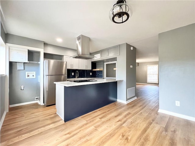 kitchen with ventilation hood, visible vents, a peninsula, freestanding refrigerator, and tasteful backsplash