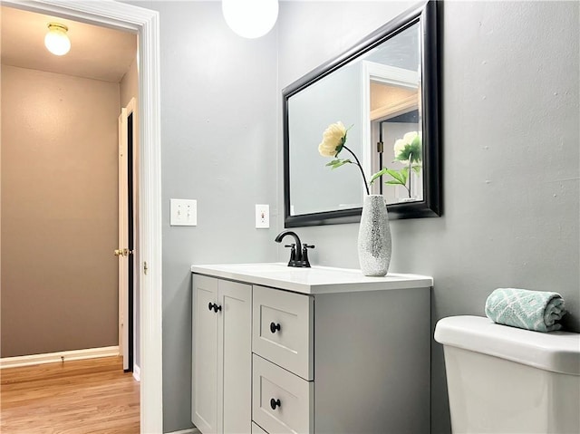 half bathroom with baseboards, toilet, wood finished floors, and vanity