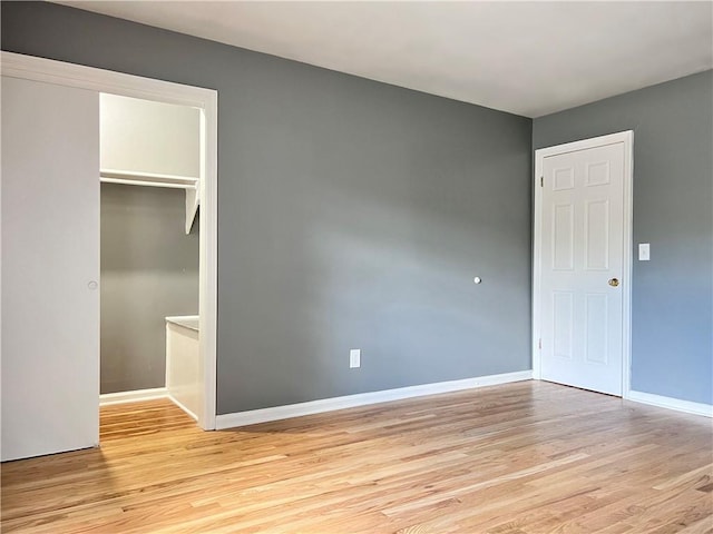 unfurnished bedroom with a closet, baseboards, light wood-style flooring, and a spacious closet