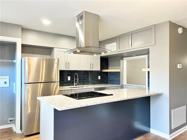 kitchen with visible vents, a peninsula, island exhaust hood, freestanding refrigerator, and decorative backsplash