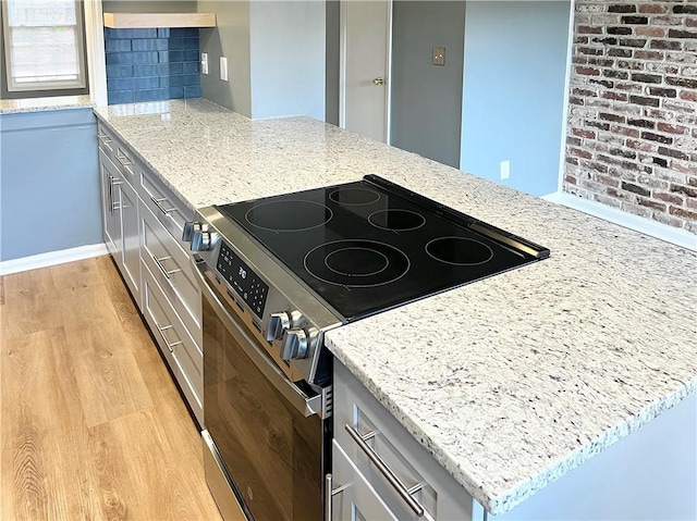 kitchen featuring electric stove, light stone counters, light wood-style floors, a peninsula, and baseboards