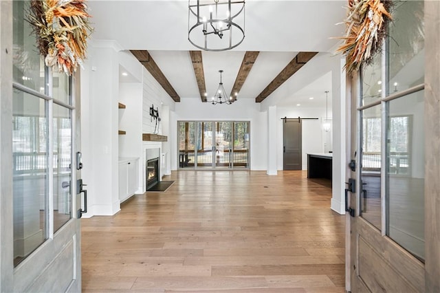 entryway with a notable chandelier, light wood finished floors, a barn door, a glass covered fireplace, and beamed ceiling