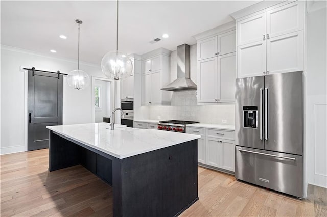 kitchen featuring a barn door, stainless steel appliances, light wood-type flooring, wall chimney range hood, and backsplash