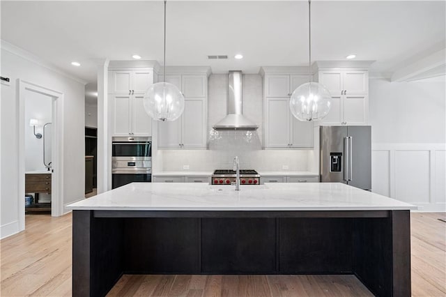 kitchen featuring light wood finished floors, tasteful backsplash, wall chimney exhaust hood, appliances with stainless steel finishes, and a sink