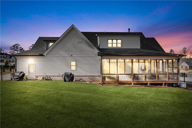 back of house at dusk featuring a yard, fence, and a sunroom