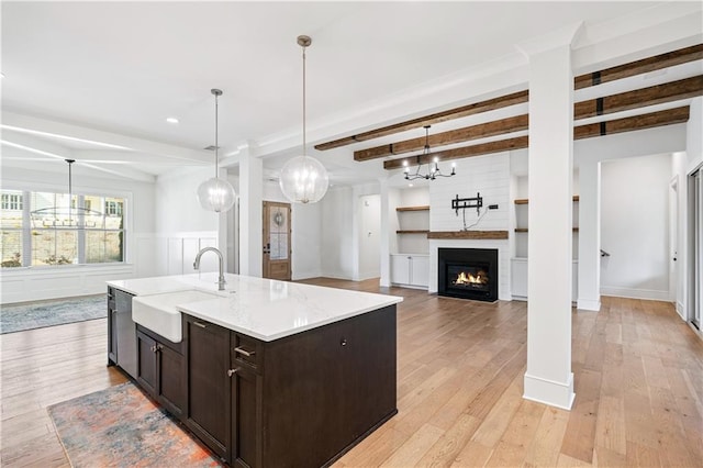 kitchen featuring stainless steel dishwasher, light wood-style flooring, beam ceiling, and a sink