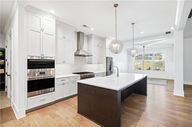 kitchen featuring appliances with stainless steel finishes, light countertops, wall chimney range hood, and light wood finished floors