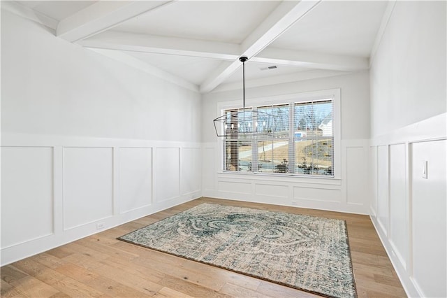 dining area with a decorative wall, beamed ceiling, and wood finished floors