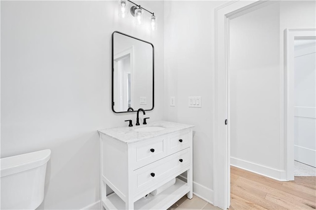 bathroom featuring toilet, wood finished floors, vanity, and baseboards