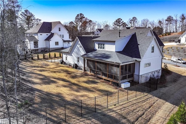 back of property featuring a shingled roof, fence, a sunroom, a lawn, and a residential view