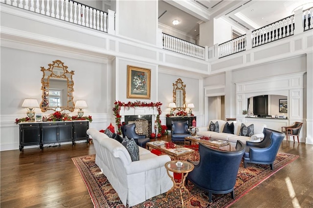 living area featuring dark wood-style floors, a fireplace, a towering ceiling, and a decorative wall