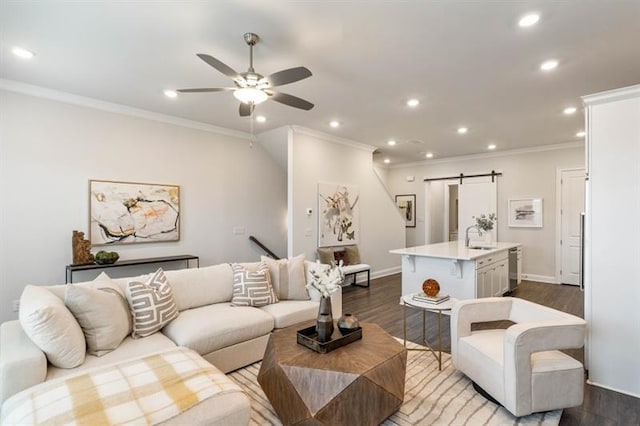 living room featuring ceiling fan, a barn door, wood-type flooring, and ornamental molding