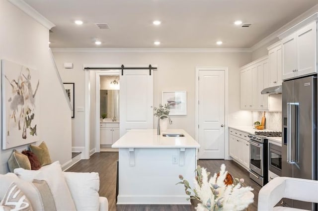 kitchen featuring sink, dark hardwood / wood-style flooring, appliances with stainless steel finishes, a barn door, and a center island with sink