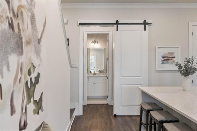 corridor with dark wood-type flooring, ornamental molding, and a barn door