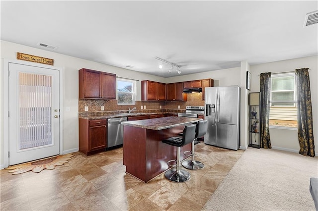 kitchen with stainless steel appliances, visible vents, a kitchen breakfast bar, tasteful backsplash, and dark countertops