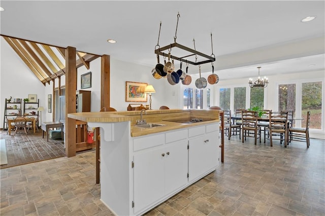 kitchen featuring sink, white cabinetry, decorative light fixtures, a chandelier, and an island with sink