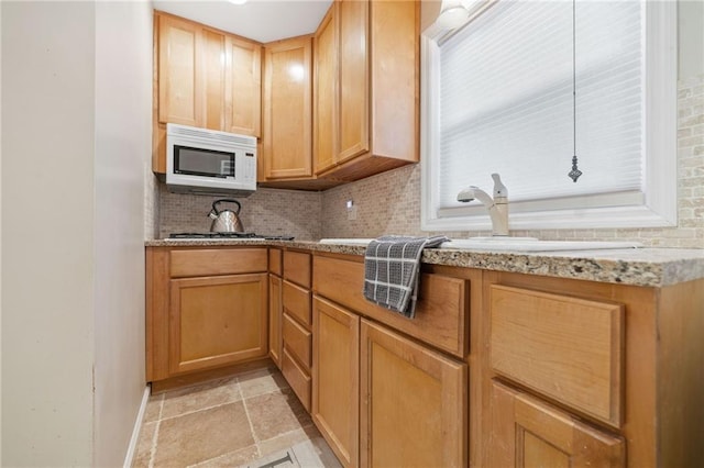 kitchen featuring stone tile floors, light stone counters, white microwave, a sink, and backsplash