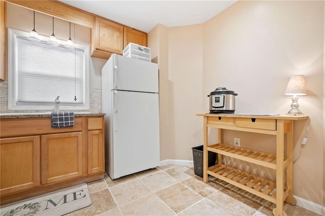 kitchen featuring baseboards, light stone counters, freestanding refrigerator, brown cabinetry, and stone finish floor