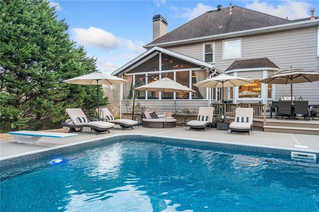 back of house with an outdoor pool, a sunroom, a shingled roof, a chimney, and a patio area