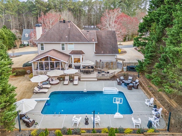 rear view of property with a fenced in pool, a sunroom, outdoor dining area, a fenced backyard, and a deck