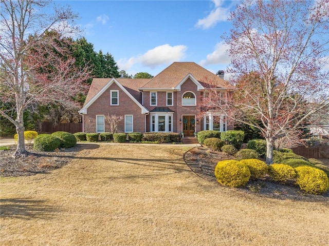 colonial inspired home with a front yard, fence, brick siding, and a chimney