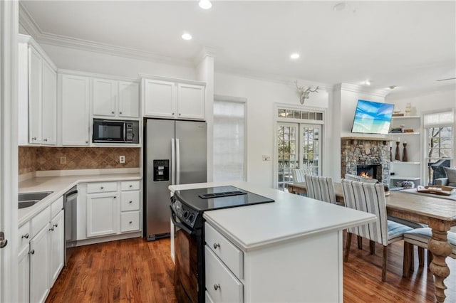 kitchen with decorative backsplash, white cabinets, black appliances, and a fireplace