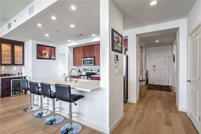 kitchen featuring a breakfast bar area, visible vents, appliances with stainless steel finishes, glass insert cabinets, and beverage cooler