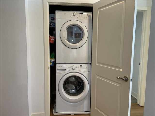 washroom with stacked washer / drying machine, laundry area, and wood finished floors