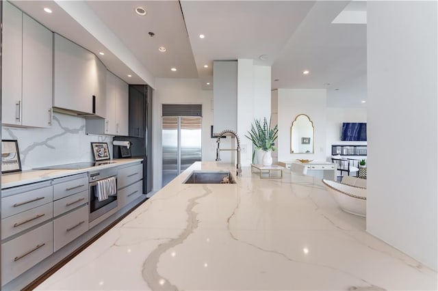 kitchen featuring gray cabinetry, stainless steel appliances, light stone counters, and a sink
