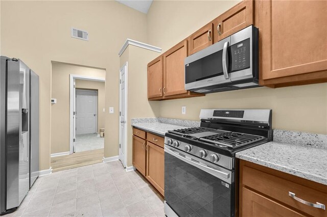 kitchen featuring light stone countertops, a towering ceiling, stainless steel appliances, and light tile patterned flooring