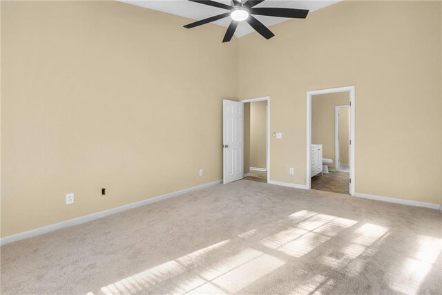 unfurnished bedroom with ceiling fan, a towering ceiling, light carpet, and ensuite bath