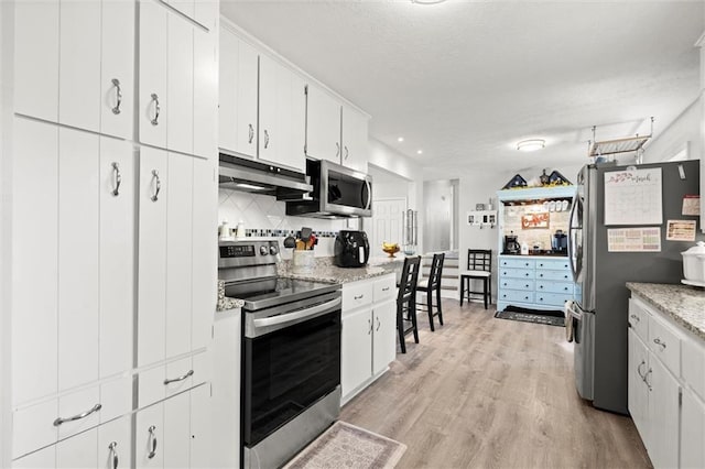 kitchen with light wood-style flooring, stainless steel appliances, white cabinets, under cabinet range hood, and backsplash