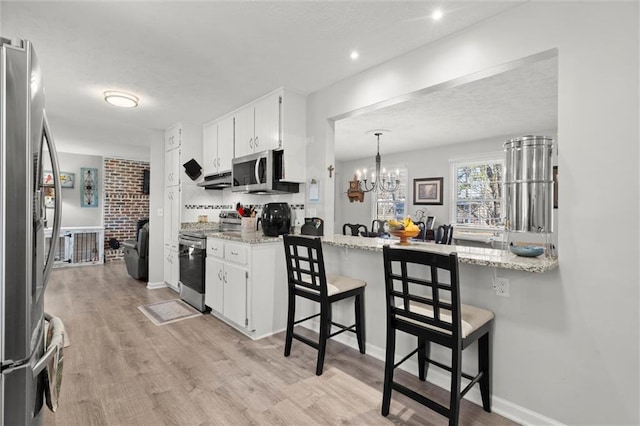 kitchen with stainless steel appliances, a kitchen bar, light wood-style flooring, and white cabinets