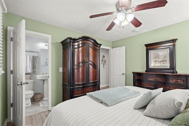 bedroom featuring a textured ceiling, wood finished floors, ensuite bath, baseboards, and ceiling fan