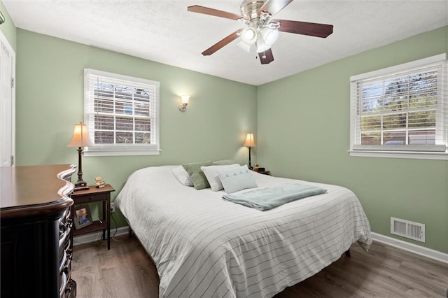 bedroom with a ceiling fan, wood finished floors, visible vents, baseboards, and a textured ceiling